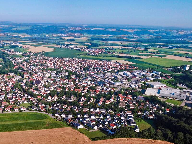 Das Bild zeigt eine Luftaufnahme einer ländlichen Gegend mit Feldern, Wäldern und einer kleinen Stadt mit vielen Häusern.