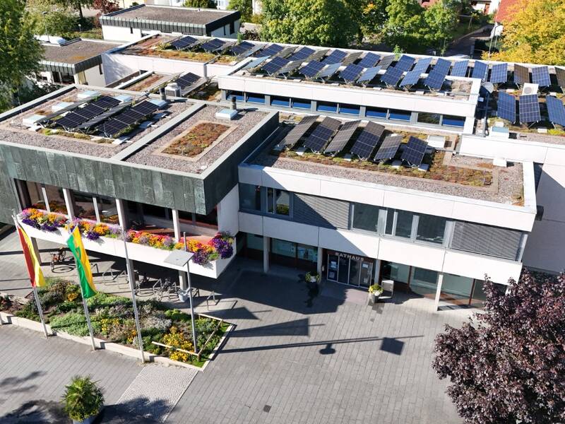 Ein modernes Gebäude mit begrüntem Dach und Solarpaneelen, umgeben von Bäumen und Flaggen.