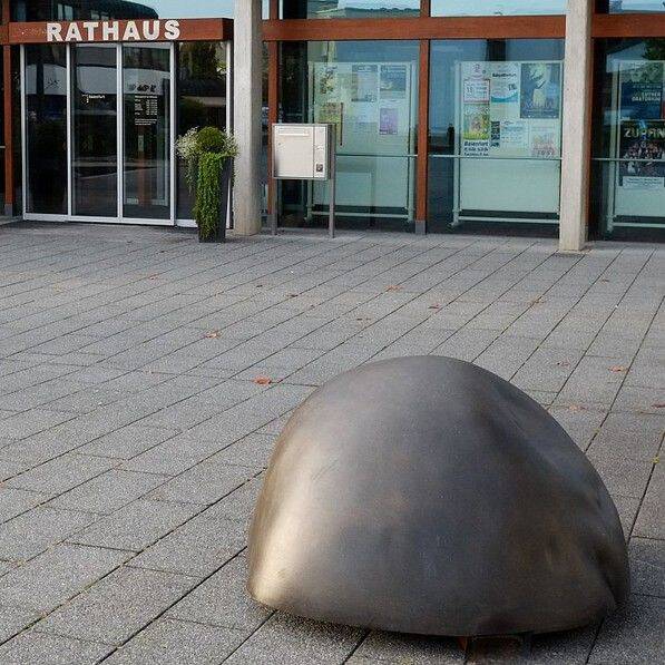 Vor dem Eingang eines Gebäudes mit der Aufschrift "Rathaus" liegt ein großer, halbrunder grauer Stein auf dem gepflasterten Platz.