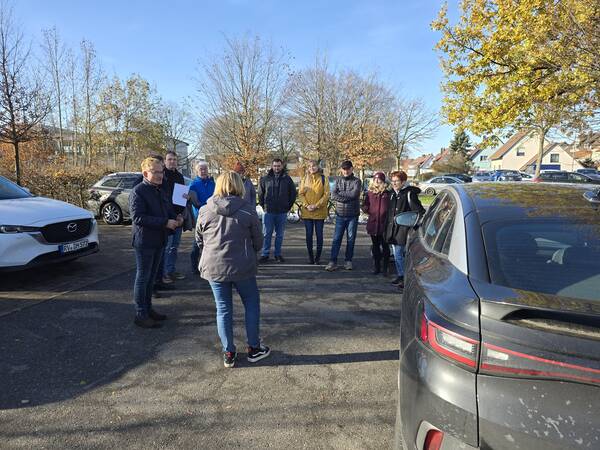 Mehrere Personen die auf einem Parkplatz vor einem Auto stehen.