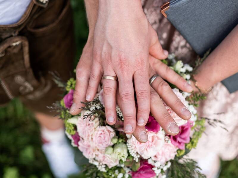 Zwei Menschen mit Eheringen halten ihre Hand über einen Blumenstrauß